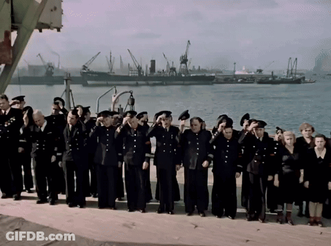 A Large Group Of People In Black Uniforms Salute In Front Of A Body Of Water GIF