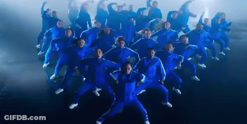 A Large Group Of People In Blue Jumpsuits Are Dancing GIF