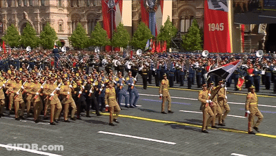 A Large Group Of Soldiers Marching Down A Street With A Banner That Says 1945 GIF