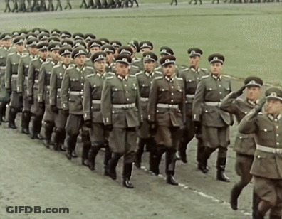 A Large Group Of Soldiers Marching In A Line With One Wearing A Hat With The Letter T On It GIF