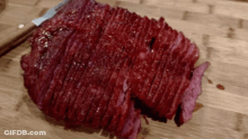 A Large Piece Of Meat Is Sitting On A Wooden Cutting Board GIF