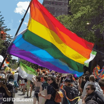 A Large Rainbow Flag Is Being Flown In A Crowded Street GIF