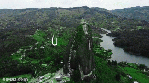 A Large Rock In The Middle Of A Lush Green Valley With The Letter U Above It GIF