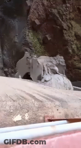 A Large Rock Is Sitting On The Side Of A Road Next To A Waterfall . GIF