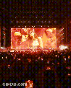 A Large Screen Shows A Group Of People On A Stage At A Concert GIF