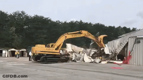 A Large Yellow Excavator Is Demolishing A Building That Says Barco On It GIF