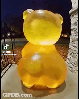 A Large Yellow Gummy Bear Is Sitting On The Sidewalk In Front Of A Building . GIF