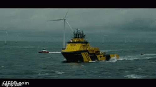 A Large Yellow Ship Is Floating In The Ocean With A Wind Turbine In The Background GIF