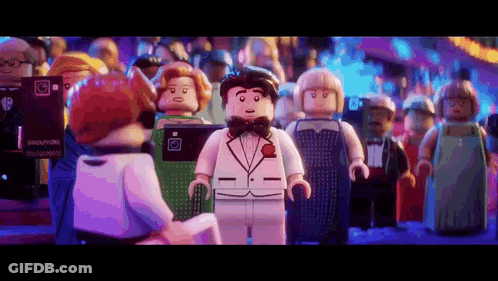A Lego Man In A Tuxedo Is Standing In Front Of A Crowd Of People . GIF