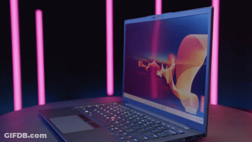 A Lenovo Laptop Is Open On A Table With Pink Lights In The Background GIF