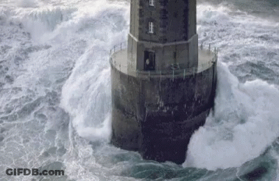 A Lighthouse In The Middle Of The Ocean With Waves Crashing Against It GIF