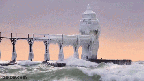 A Lighthouse Is Covered In Ice And Waves Crashing Against It GIF