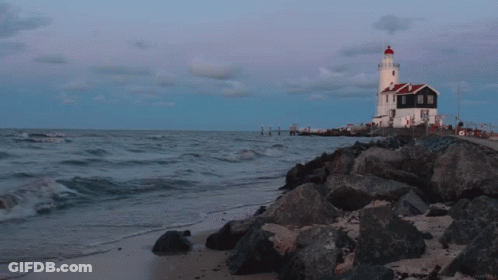 A Lighthouse Sits On A Rocky Shoreline Near The Ocean GIF