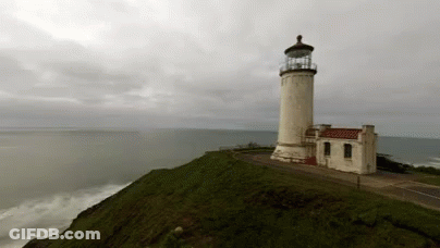 A Lighthouse Sitting On Top Of A Hill Overlooking The Ocean GIF