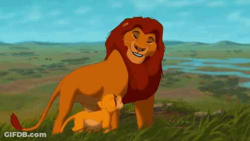 A Lion And A Cub Standing In The Grass GIF