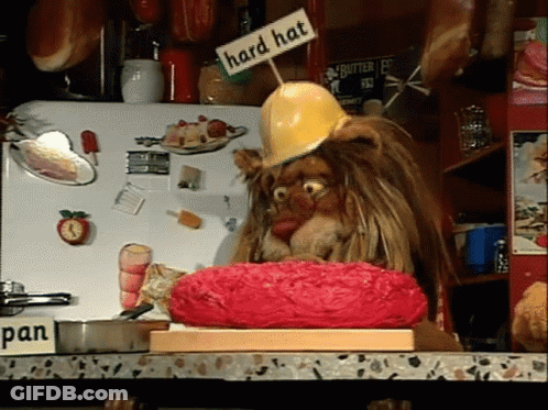 A Lion Wearing A Hard Hat Is Sitting On A Cutting Board GIF