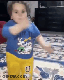 A Little Boy In A Blue Shirt And Yellow Pants Is Dancing On A Rug . GIF