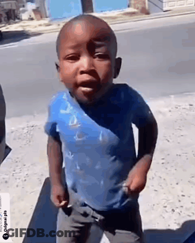 A Little Boy In A Blue Shirt Is Standing On The Sidewalk . GIF