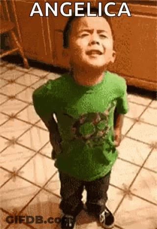 A Little Boy In A Green Shirt Is Standing On A Tiled Floor With The Name Angelica On The Bottom . GIF