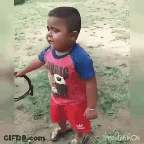 A Little Boy In A Pink Shirt And Red Shorts Is Holding A Tambourine In His Hand . GIF