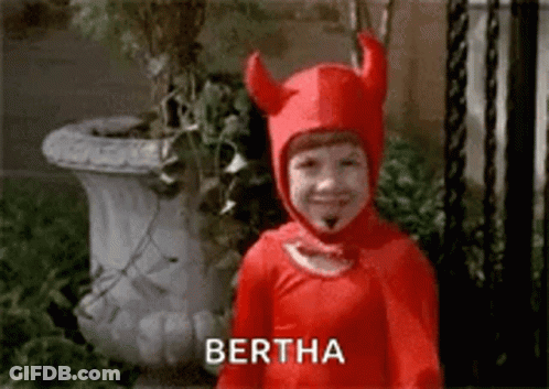 A Little Boy In A Red Devil Costume Is Smiling And Standing In Front Of A Potted Plant . GIF