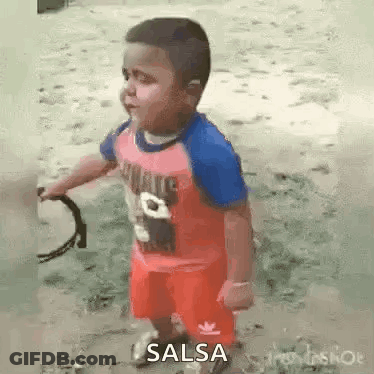 A Little Boy In A Red Shirt And Red Shorts Is Holding A Tambourine In His Hands . GIF