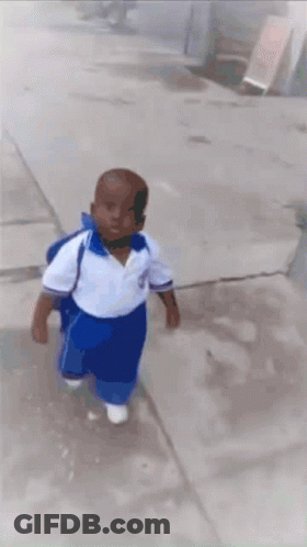 A Little Boy In A White Shirt And Blue Pants Is Walking Down A Sidewalk GIF