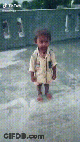 A Little Boy In A Yellow Shirt Is Standing In A Puddle Of Water GIF