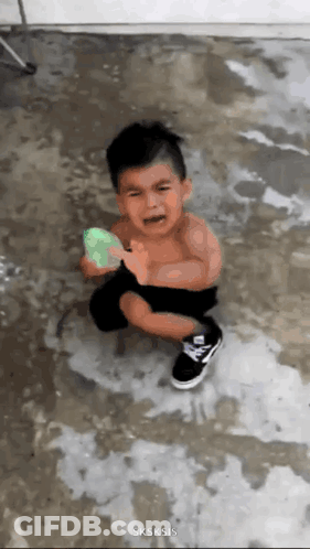 A Little Boy Is Crying While Holding A Green Water Balloon . GIF