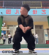A Little Boy Is Dancing In Front Of A Building That Says Tiktok GIF