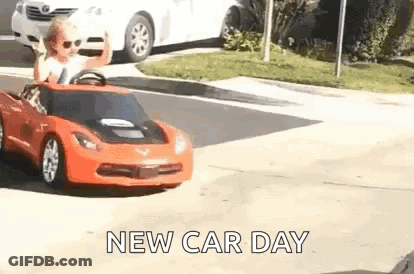 A Little Boy Is Driving A Red Toy Car Down The Street . GIF
