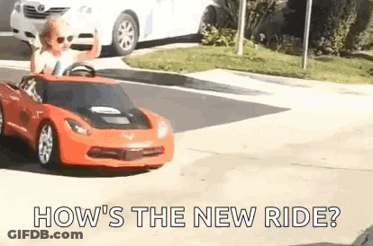 A Little Boy Is Driving A Red Toy Car Down The Street . GIF