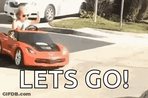 A Little Boy Is Driving A Red Toy Car On A Street . GIF