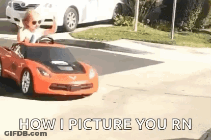 A Little Boy Is Driving A Red Toy Car On A Street . GIF