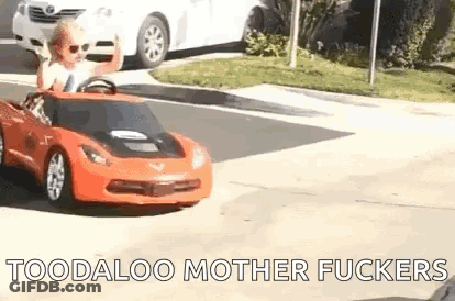 A Little Boy Is Driving A Red Toy Car On A Street . GIF