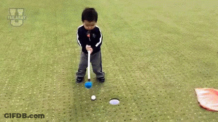 A Little Boy Is Laying On The Ground On A Golf Course Next To A Flag And A Golf Club . GIF