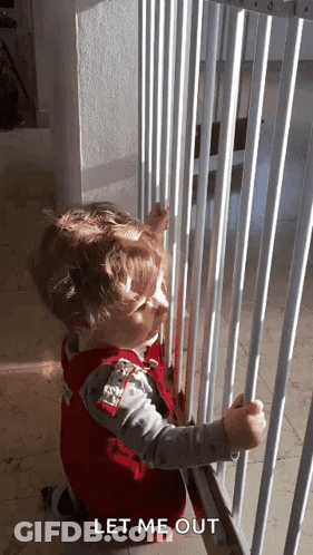 A Little Boy Is Looking Through A Fence With The Words Let Me Out Below Him . GIF