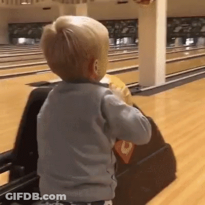 A Little Boy Is Playing In A Bowling Alley With A Bowling Ball . GIF