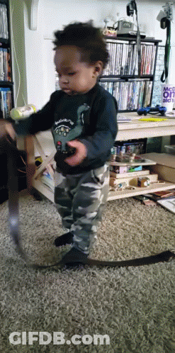 A Little Boy Is Playing With A Remote Control In Front Of A Sign That Says " Make It " GIF
