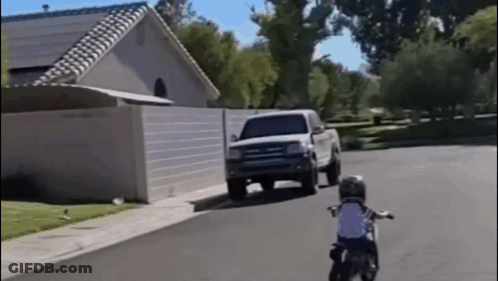 A Little Boy Is Riding A Motorcycle Down A Street GIF