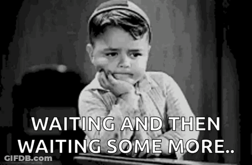 A Little Boy Is Sitting At A Desk With His Hand On His Chin And The Words `` Waiting And Then Waiting Some More '' . GIF