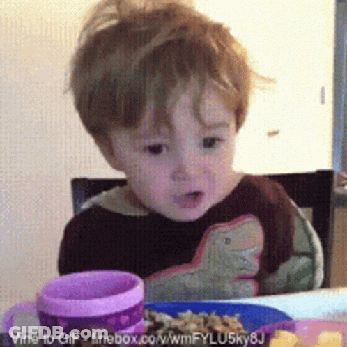 A Little Boy Is Sitting At A Table With A Plate Of Food And A Pink Cup GIF