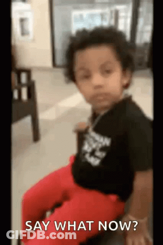 A Little Boy Is Sitting In A Chair With The Words `` Say What Now '' Written On The Screen . GIF