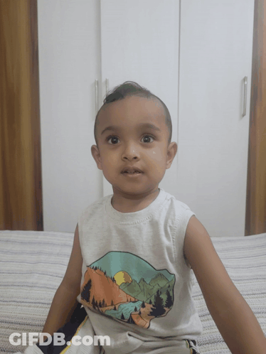 A Little Boy Is Sitting On A Bed Wearing A White Tank Top With Mountains On It GIF