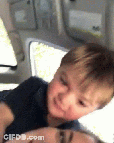 A Little Boy Is Sitting On The Back Of A Woman In A Car . GIF