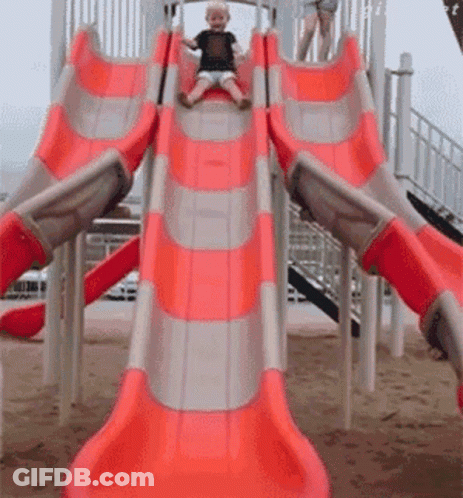 A Little Boy Is Sliding Down A Red And Gray Slide GIF