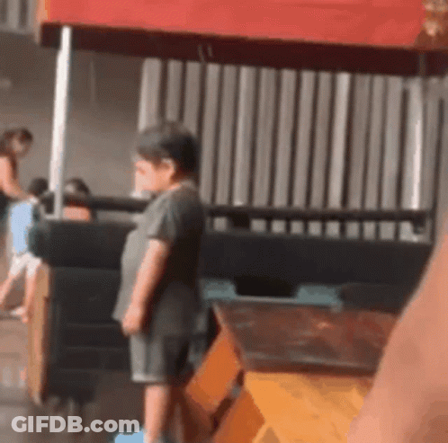 A Little Boy Is Standing In Front Of A Red Canopy . GIF