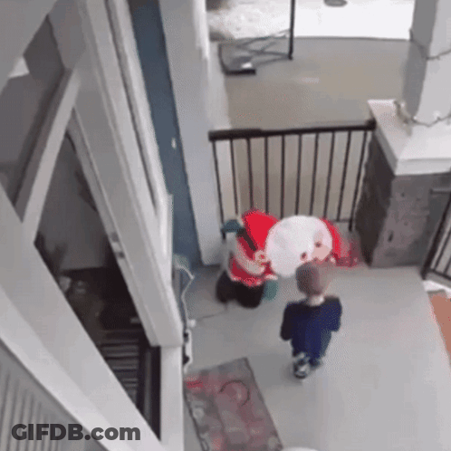 A Little Boy Is Standing Next To A Stuffed Santa Claus In A House . GIF