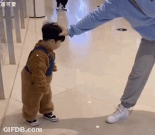 A Little Boy Is Standing Next To A Woman And Touching Her Head . GIF