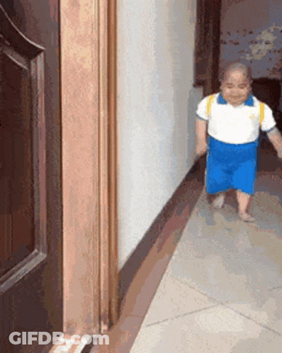 A Little Boy Is Walking Down A Hallway Next To A Door GIF